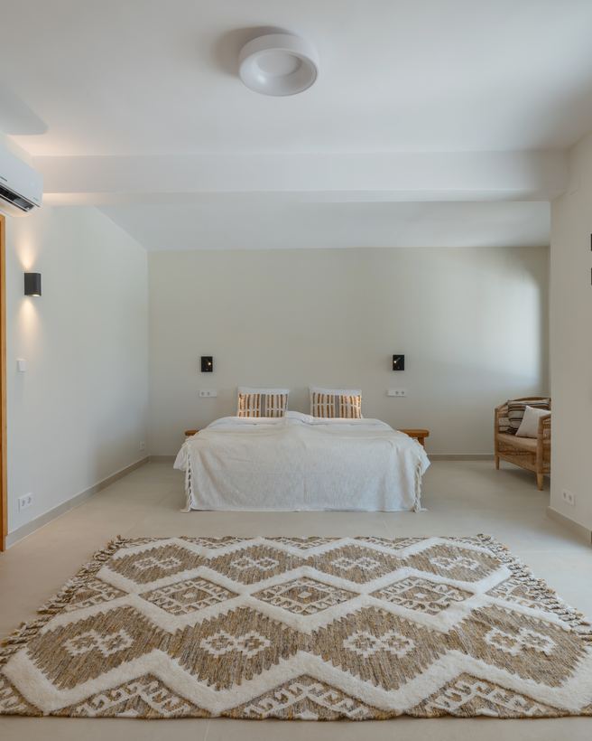 Slaapkamer met opgemaakt bed en een berbertapijt op een lichte vloer