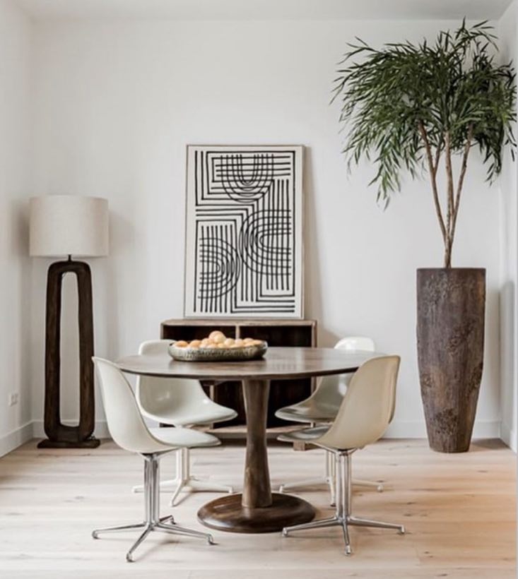 Eethoek met ronde houten tafel, witte kuipstoelen en een grote plant