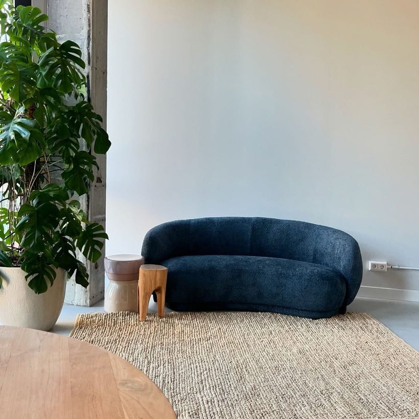 Donkerblauwe ronde bank op een jute vloerkleed naast een grote monstera