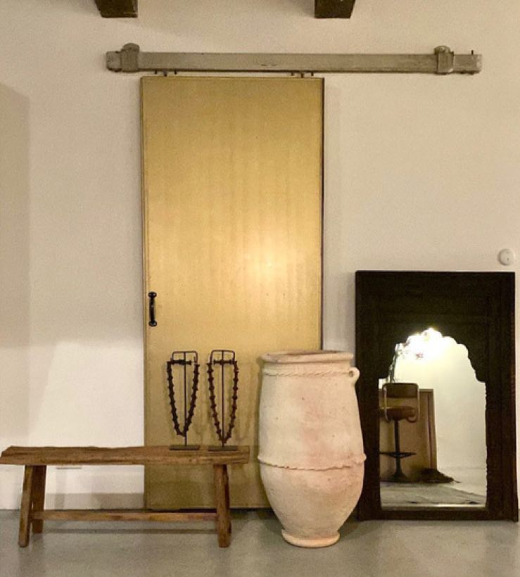 Houten bank met terracotta kruik en spiegel tegen een lichte wand