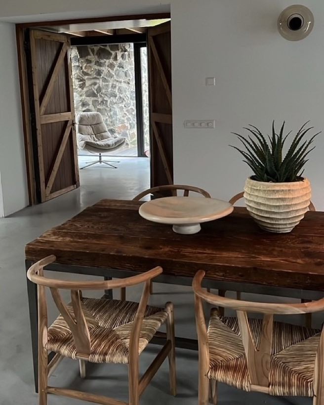 Eettafel van massief hout met rieten stoelen en uitzicht op een binnenplaats