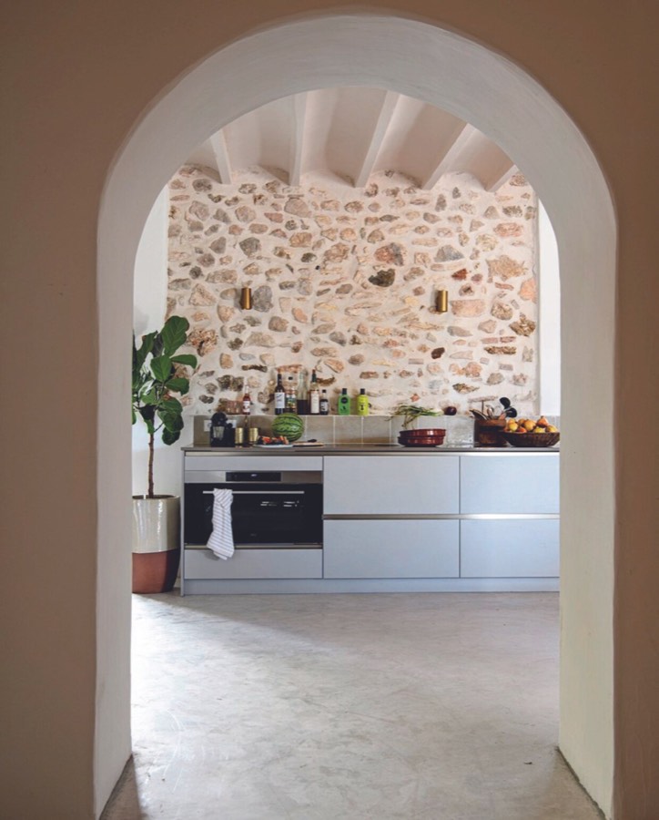 Doorkijk door een gepleisterde boog naar de keuken met natuurstenen wand