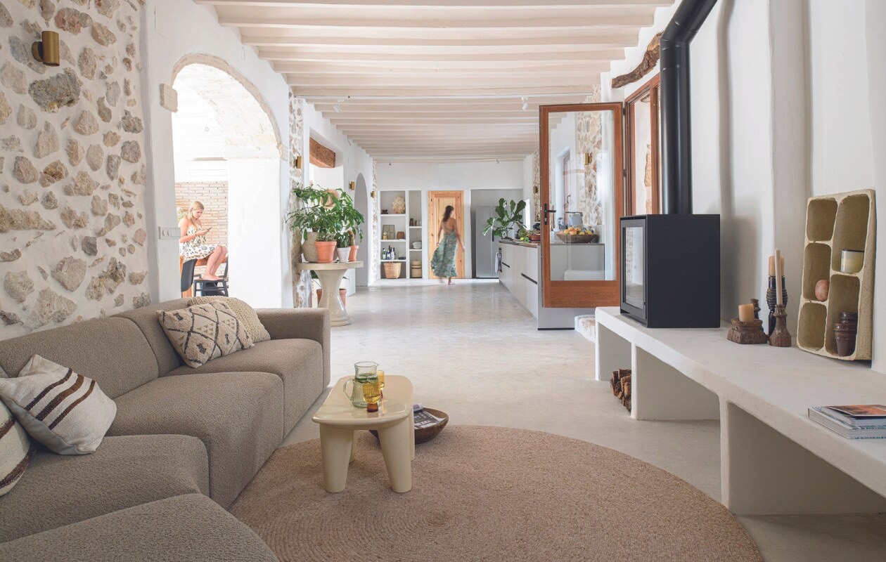Woonkamer in Torre Carrals met natuurstenen muur, witte balken en doorkijk naar de keuken